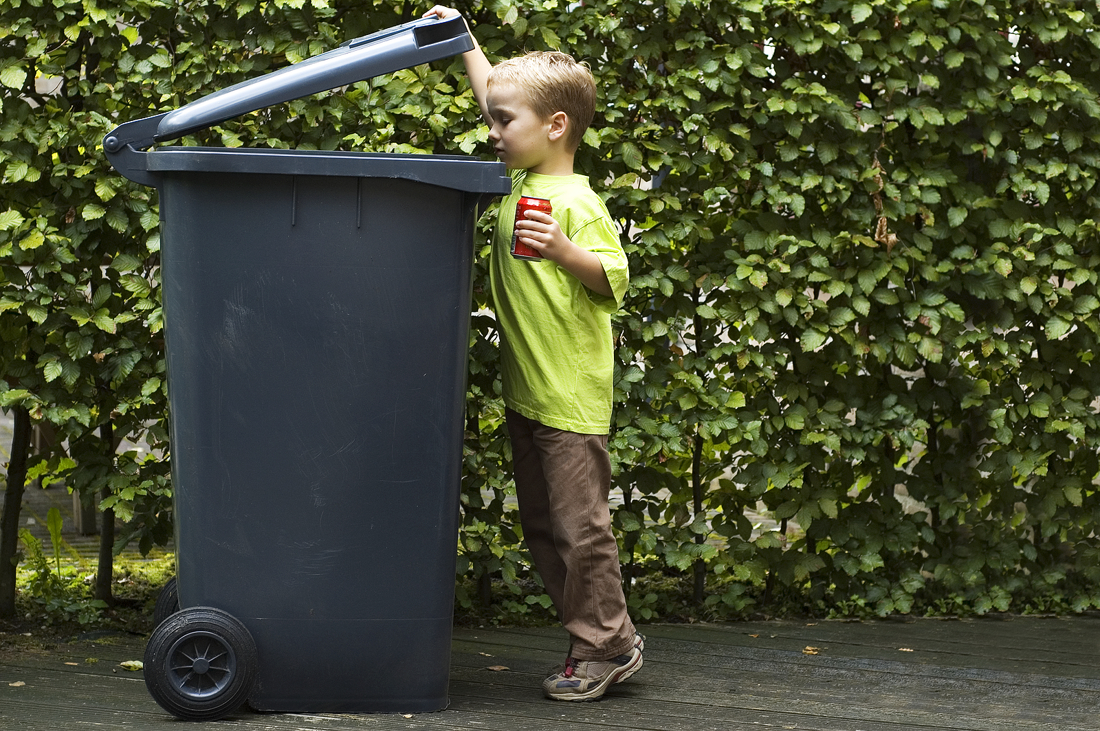 Boy wanting to throw a can in the container he is learning to be aware that recycling is important.