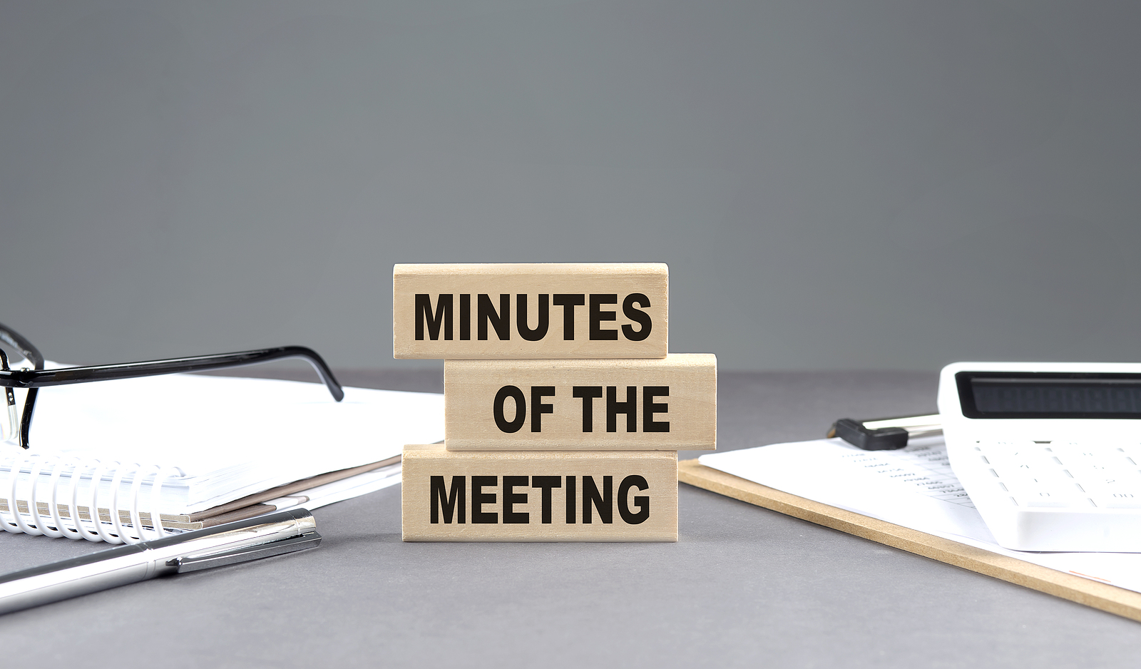 MINUTES OF THE MEETING text on a wooden block with notebook,chart and calculator, grey background
