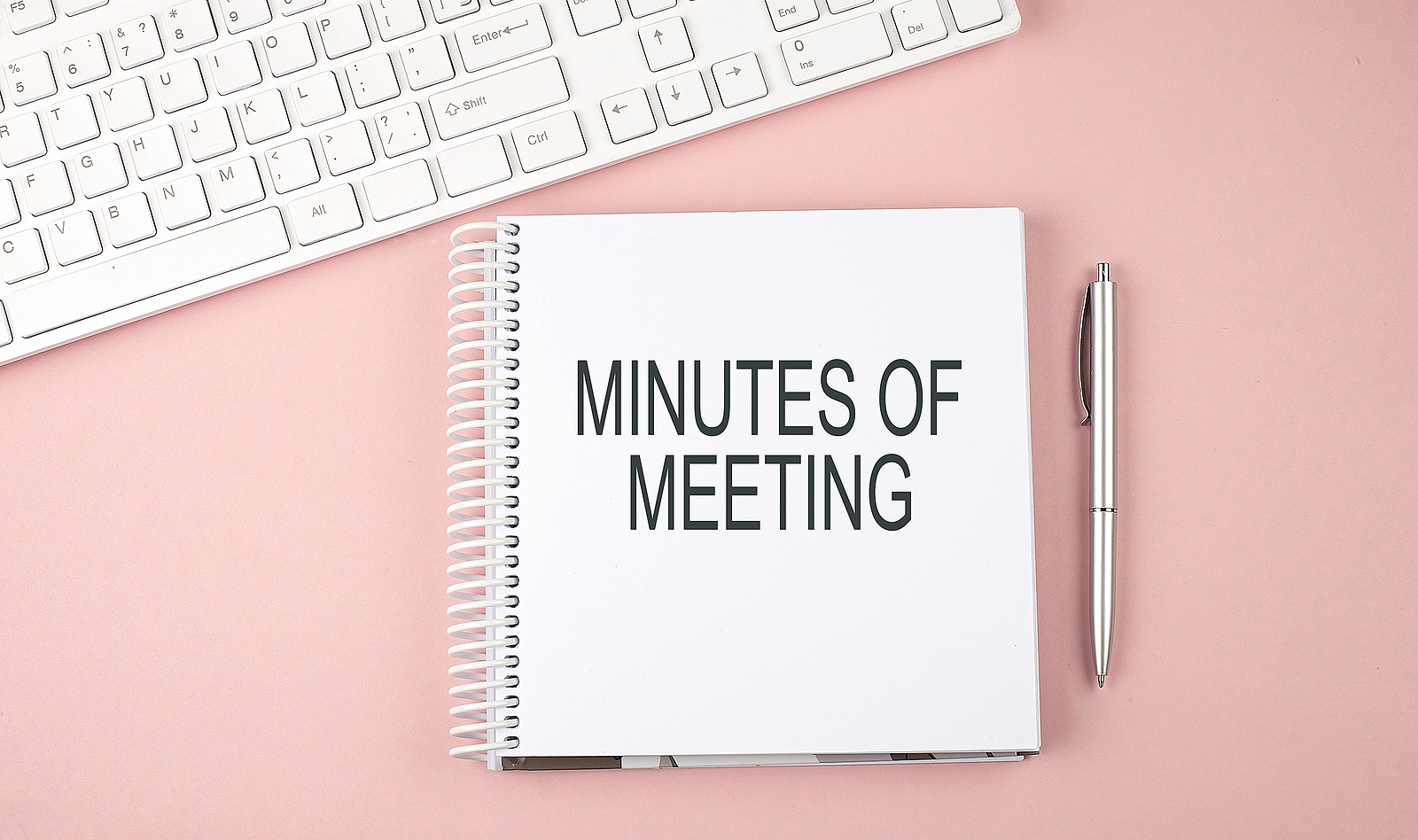 Pink office desk with keyboard and notebook , text MINUTES OF THE MEETING