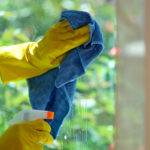 Close-up of woman cleaning window using detergent and rags. House cleaning, housekeeping and spring-cleaning concept