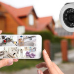 Home security system. Woman monitoring CCTV cameras on smartphone near her house, closeup