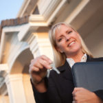 Female Real Estate Agent Handing Over Keys in Front of Beautiful House.