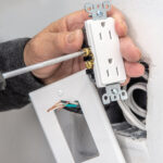 An electrician connects electrical wires to an outlet before installing it.
